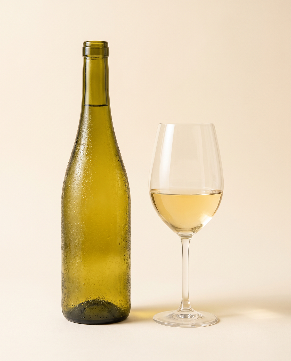 Botella de vino blanco fría junto a una copa servida