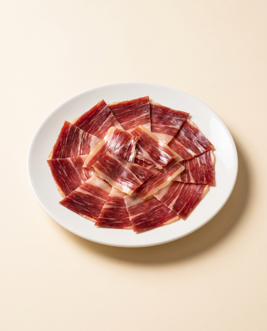 Lonchas de jamón ibérico de bellota cortadas a cuchillo, en abanico sobre plato blanco