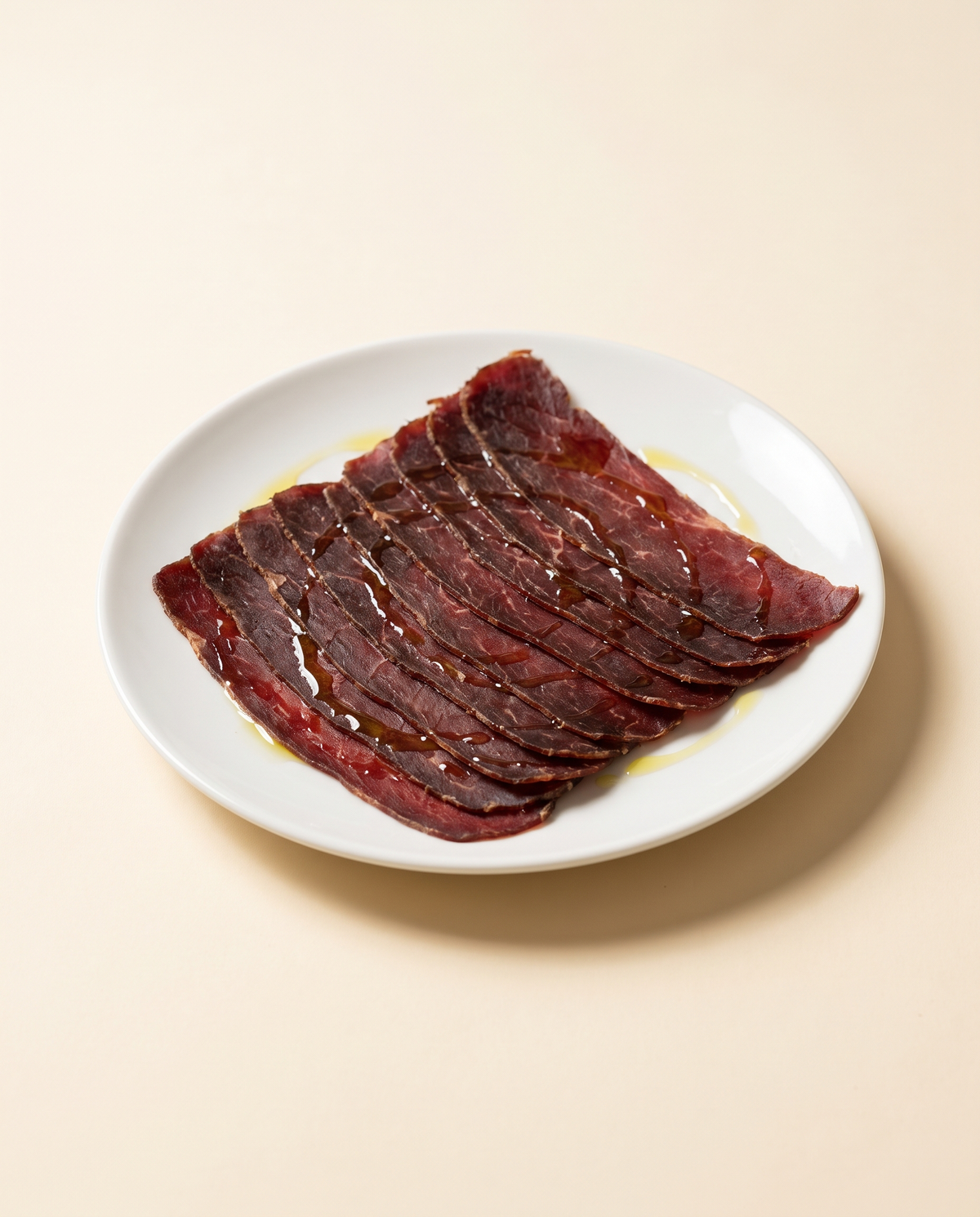 Lonchas finas de cecina de León sobre plato blanco, con un hilo de aceite de oliva