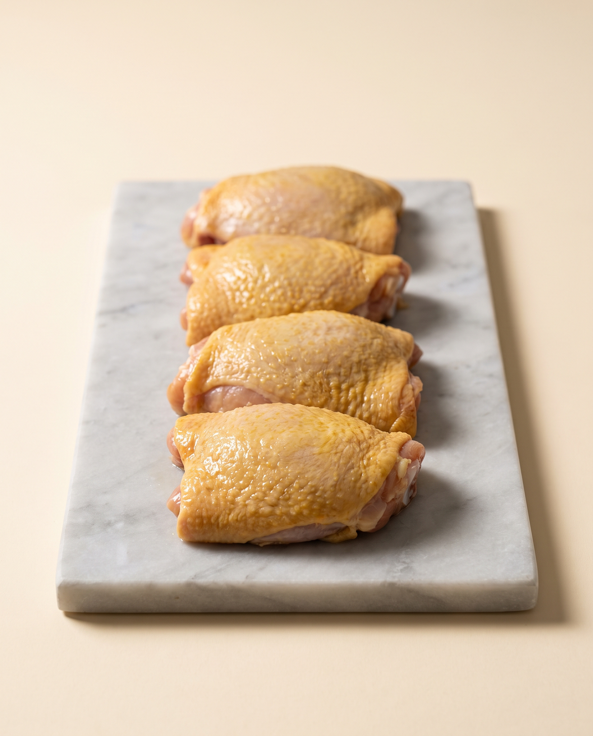 Cuatro contramuslos de pollo deshuesados con piel, abiertos en fila