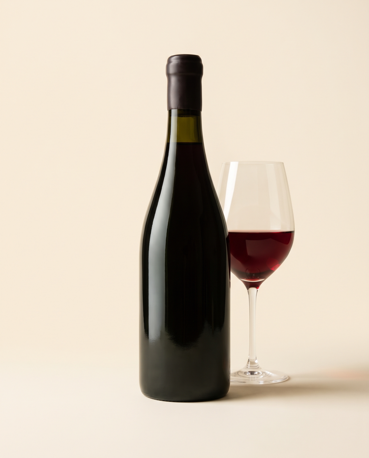 Botella de vino tinto junto a una copa servida