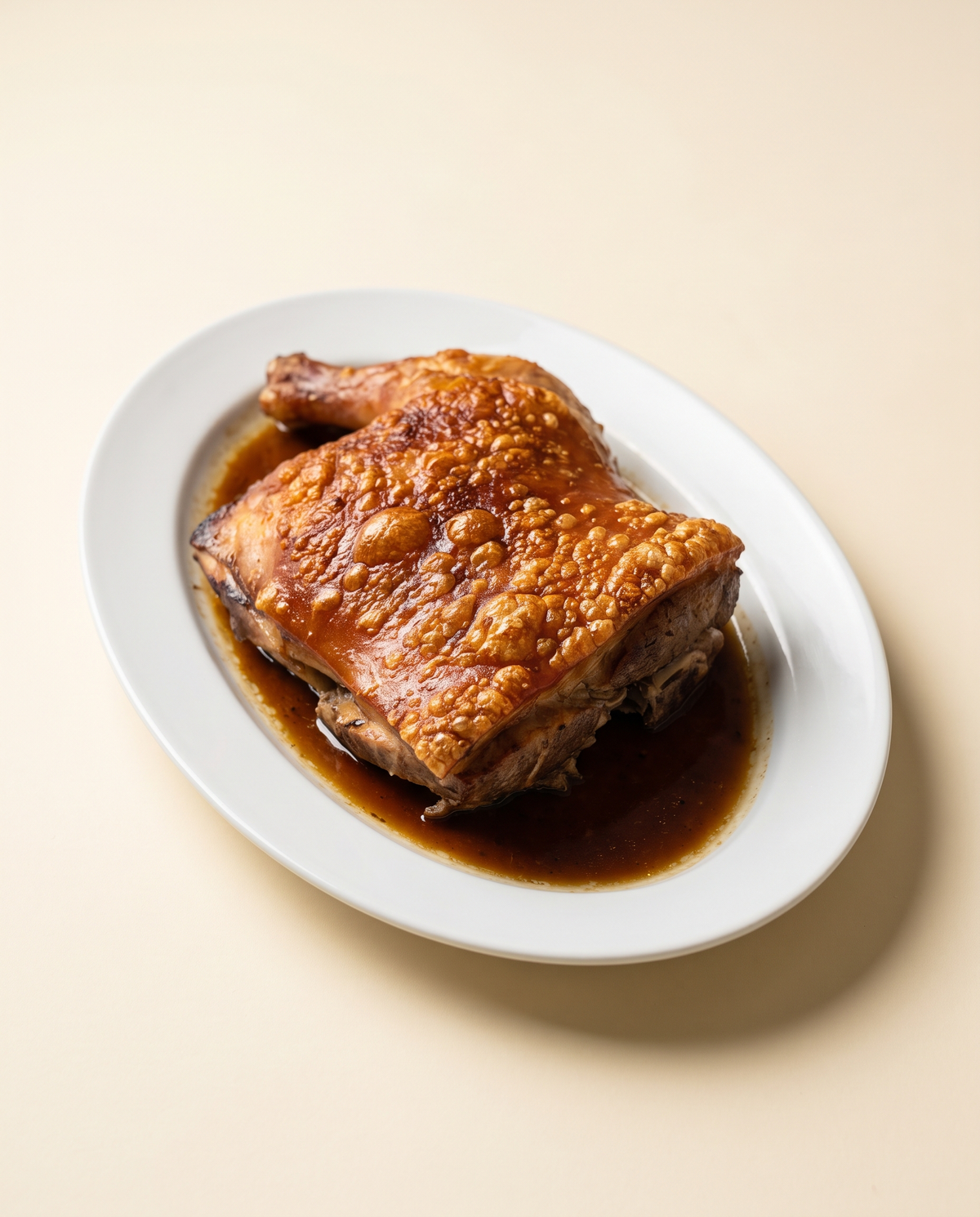 Cuarto de cochinillo confitado con la piel dorada y crujiente, en fuente blanca